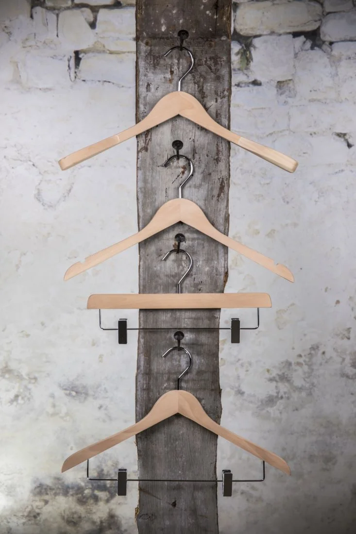 Drei naturfarbene Holzbügel mit mittelrem Hosenbügel und Clips, vertikal angeordnet – dekorativ und platzsparend.