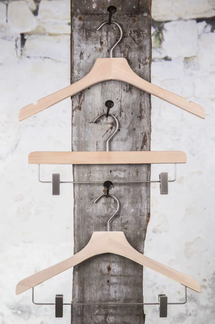 Drei naturabene Holzbügel vertikal aufgehängt an einer Wandhalterung mit Metallclip – Dekorative und platzsparende Präsentation.
