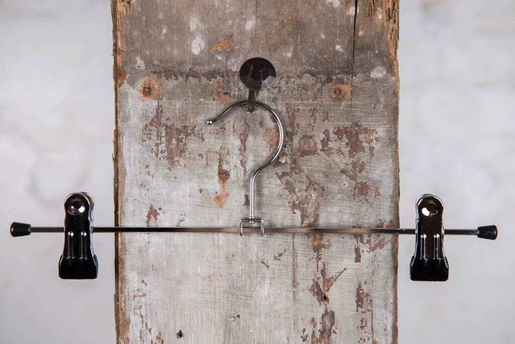 Metal trouser hanger with metal rod and clips in front of rustic wooden wall - Functional hanger for professional presentation of trousers (clamp hanger).