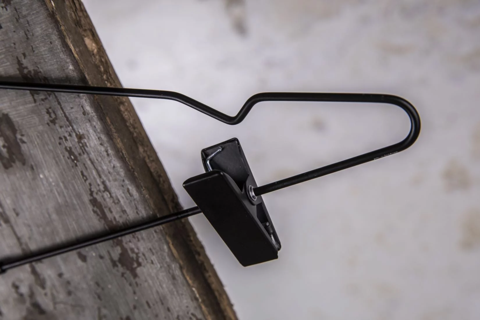 Black metal hanger with wide shoulders and clip seen from the side - Robust construction with practical clamp for professional presentation of trousers or skirts in stores and showrooms (clamp hanger)