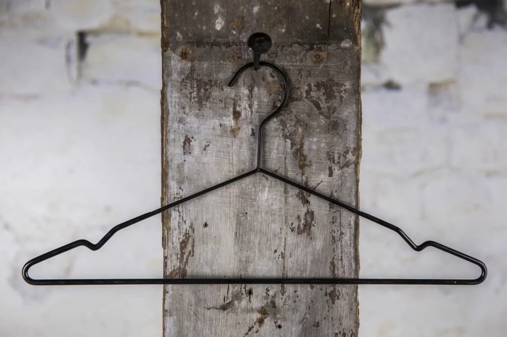 Schwarzer Drahtbügel mit leichter Schulterform, aufgehängt am Wandhaken – klassischer Kleiderbügel für den Einzelhandel.