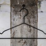 Schwarzer Drahtbügel mit leichter Schulterform, aufgehängt an Wandhaken – Klassischer Kleiderbügel für den Einzelhandel.