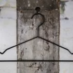Schwarzer Drahtbügel mit leichter Schulterform, aufgehängt an Wandhaken – Klassischer Kleiderbügel für den Einzelhandel.
