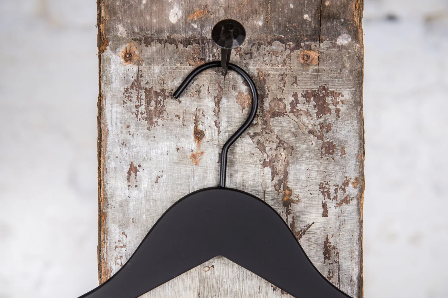 Schwarzer Kleiderbügel mit breiten Schultern, an rustikaler Wand aufgehängt – Geeignet für formelle und schwere Kleidung.