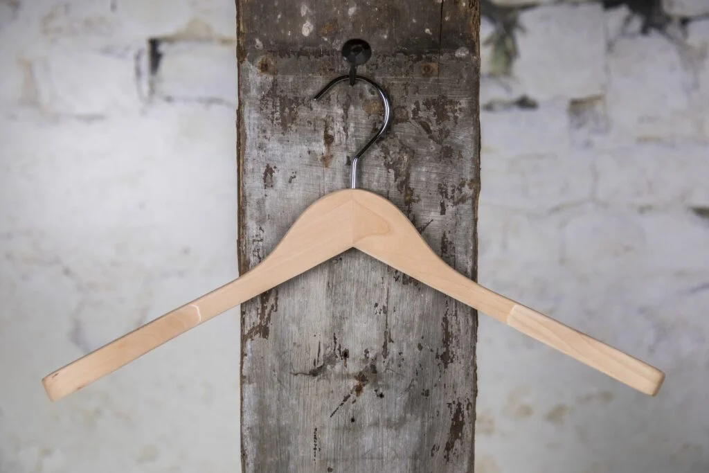 Naturholz-Kleiderbügel mit elegantem Schwung, an die Wand gehängt - klassischer Holzbügel für die anspruchsvolle Präsentation.
