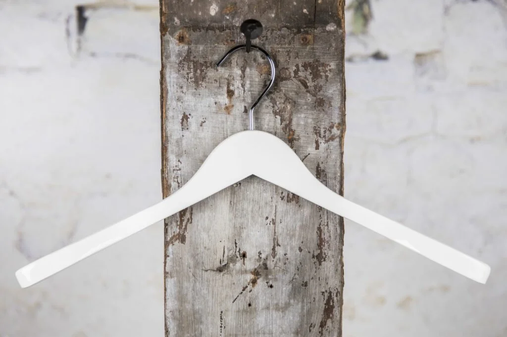Weißer, geschwungener Kleiderbügel am Wandhaken - schlichtes, modernes Design für Kleidung.