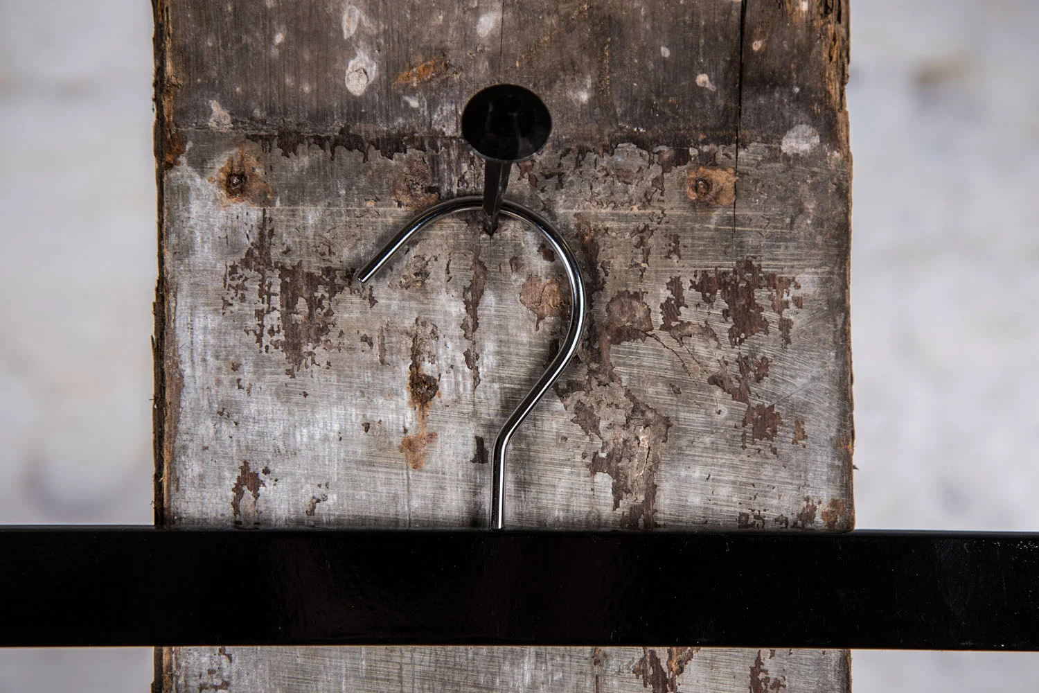 Schwarzer Hosenbügel mit silbernem Haken, frontal aufgehängt an rustikaler Holzwand – Schlicht und professionell.