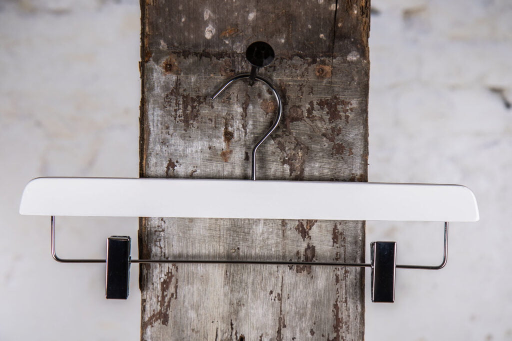 Weißer Hosenbügel mit schwarzer Metalstange und Klammern – Kontrastreiches Design für moderne Einrichtung.