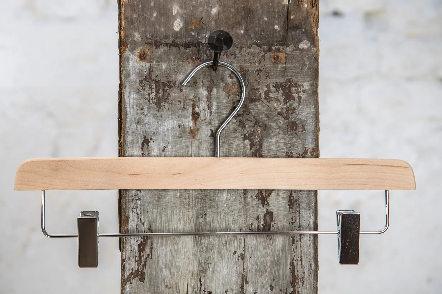 Hosenbügel aus Naturholz mit silberner Metallstange und schwarzen Clips – Kombination aus Naturmaterial und Funktionalität.