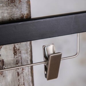 Detailaufnahme eines silbernen Clips an schwarzem Bügel – Materialkontrast zwischen Holz und Metall.