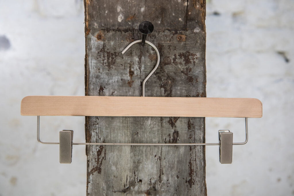 Schlichter Hosenbügel aus Naturholz mit silberner Metallstange und Clips – minimalistisches Design zur Hosenpräsentation.