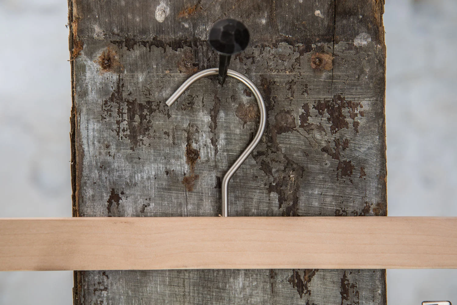 Heller Holzbügel mit silbernem Metallhaken, aufgehäng an rustical Wall – Klassischer Hosenbügel für strukturierte Präsentation.