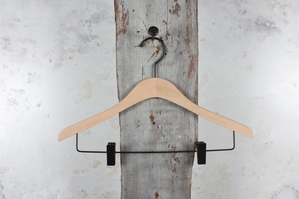 Wooden trouser hanger with black clips, hung on a wooden board - Classic clamp hanger with a stable hold.