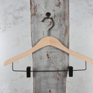 Holzkleiderbügel mit schwarzen Clips, aufgehängt an Holzplatte – Klassischer Hosenbügel mit stabilem Halt.