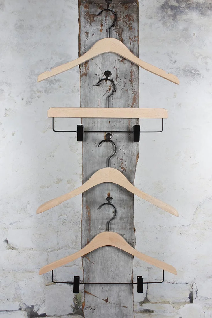 Four Holzkleiderbügel vertikal an schwarzer Wandhalterung – Stylish storage solution with contrast.