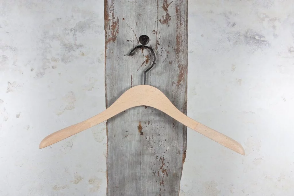 Naturfarbener Holzbügel mit sanfter Rundung am Wandhaken – klassisches Design für die professionelle Präsentation von Jacken in Geschäft und Showroom (Jackenbügel)