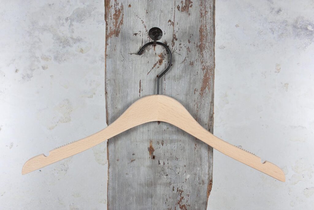 Natural colored clothes hanger with curved shoulders, aufgehäng an Wallhaken – Klassischer Holzbügel für den Einzelhandel.