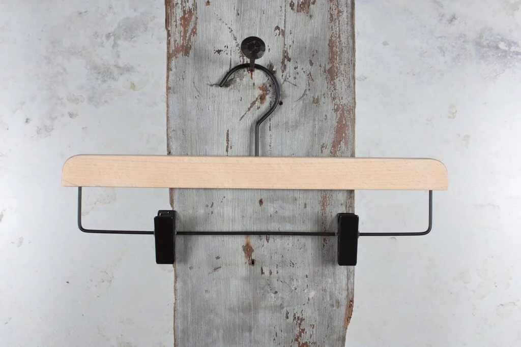Træbuksebøjle i naturfarve med sorte clips foran rustik væg – Klassisk design til detailhandel (klemmebøjle).