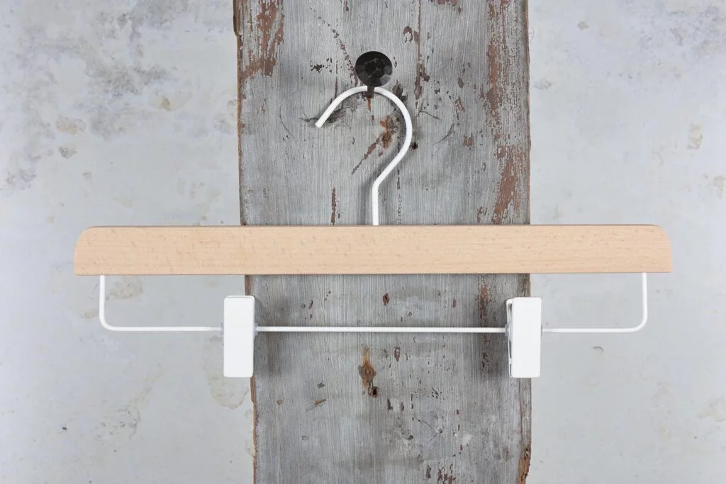 Hosenbügel aus Holz mit weißen Clips am Wandhaken – minimalistische Kombination aus Holz und Metall (Clipbügel).